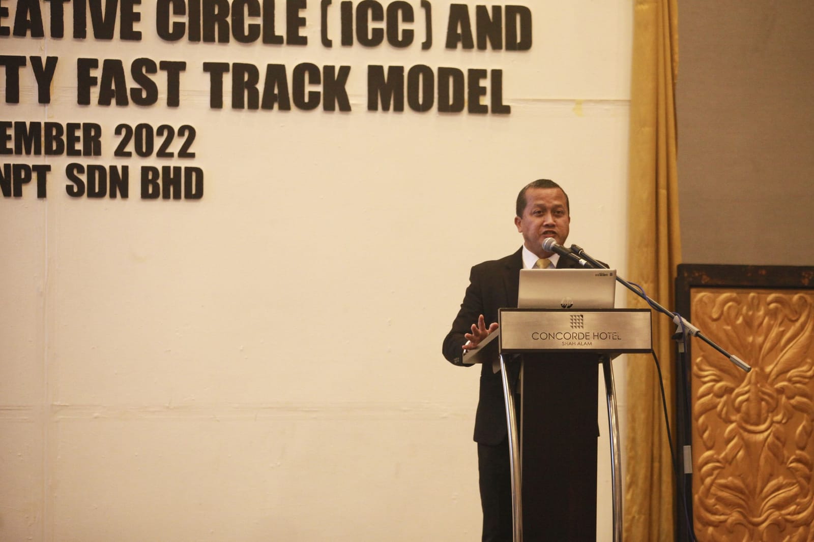 The speaker at the podium, the workshop title on the backdrop behind him